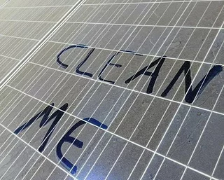 Verschmutztes Solarmodul mit der Aufschrift Clean me im Staub